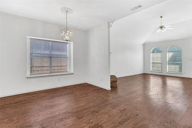 an empty room with wooden floor chandelier and windows