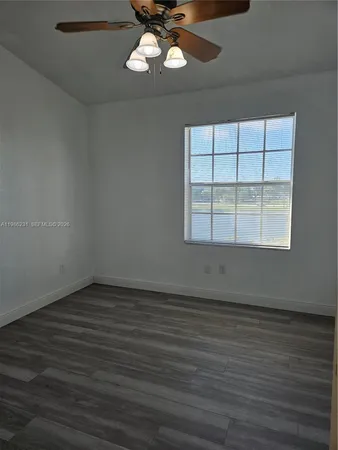 an empty room with wooden floor chandelier fan and windows