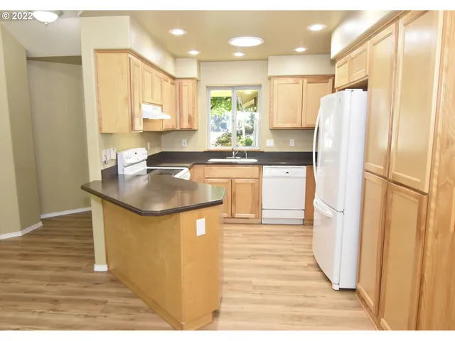 a kitchen with stainless steel appliances granite countertop a refrigerator a sink a stove and white cabinets with wooden floor