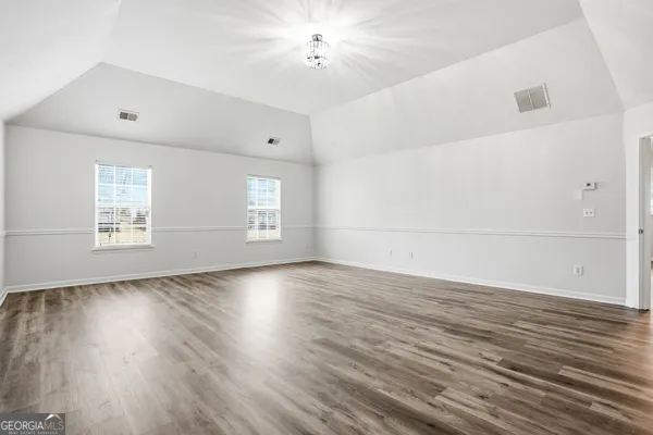 an empty room with wooden floor chandelier and windows