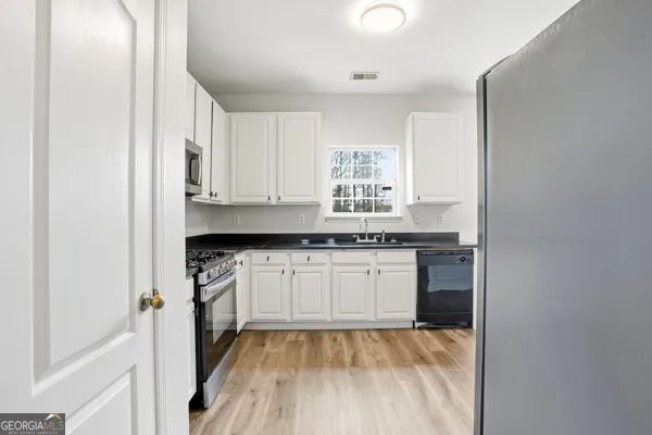 a kitchen with granite countertop a sink cabinets stainless steel appliances and a window