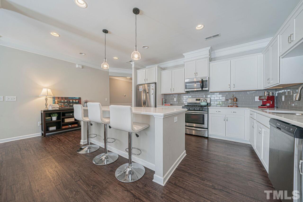 6343 Grace Lily Drive Raleigh, NC 27607 - Photo 6 of 24 a kitchen with stainless steel appliances kitchen island granite countertop a stove a sink a refrigerator and white cabinets with wooden floor
