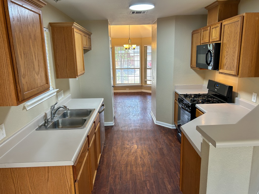 1604 Harness Race Way Pflugerville, TX 78660 - Photo 6 of 25 a kitchen that has a sink a microwave oven a stove and white cabinets with wooden floor