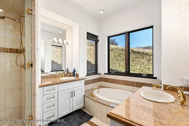 a bathroom with a granite countertop tub a double vanity sink a window and a shower