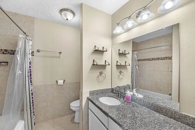 a bathroom with a granite countertop shower sink vanity mirror and toilet
