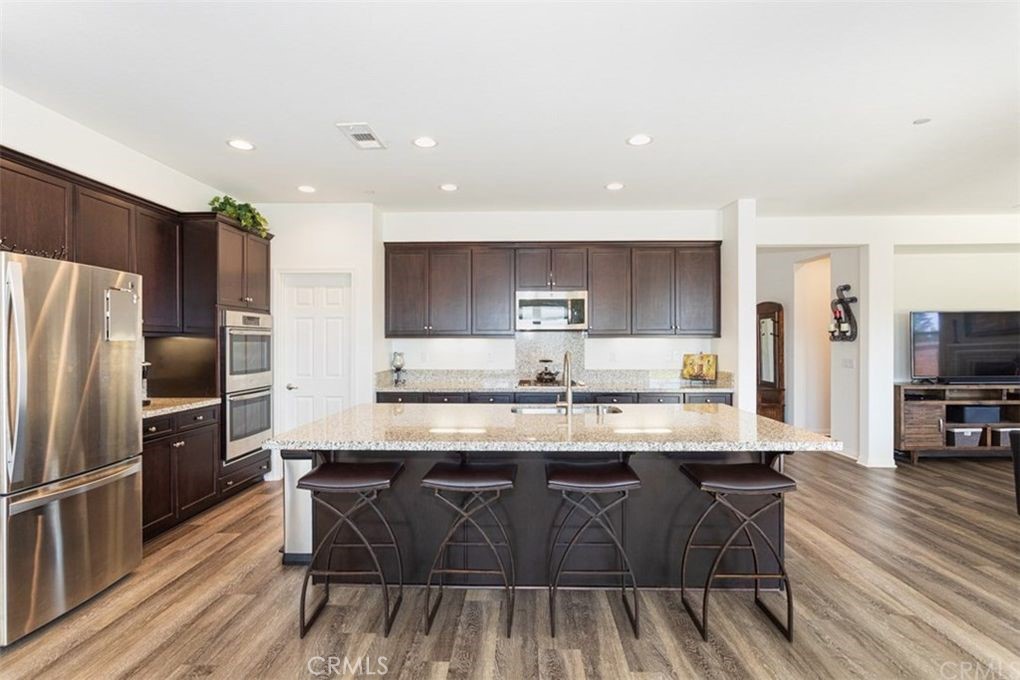 a kitchen with stainless steel appliances granite countertop a sink a stove a refrigerator and island with wooden floor