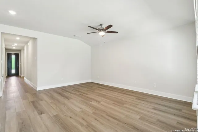 an empty room with wooden floor a ceiling fan and entryway