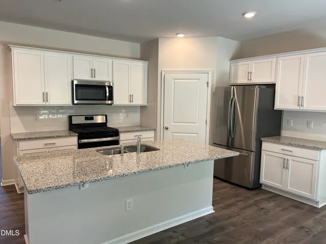 a kitchen with stainless steel appliances granite countertop a refrigerator a stove a sink a microwave and white cabinets