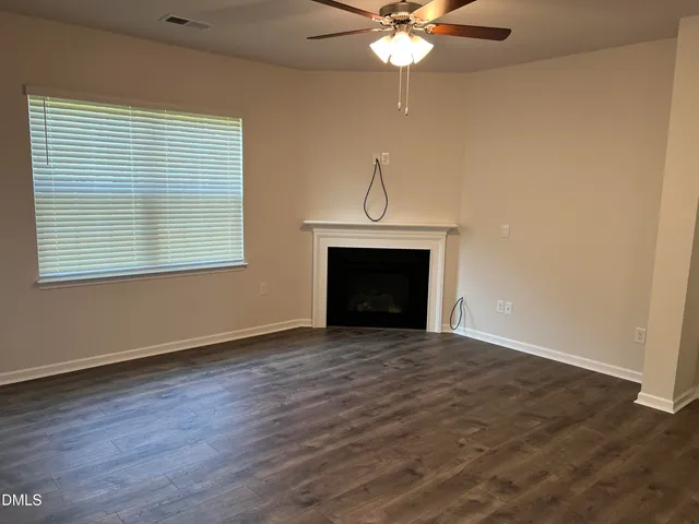 an empty room with wooden floor a ceiling fan and a fireplace