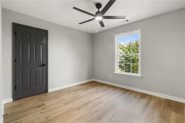an empty room with wooden floor ceiling fan and windows
