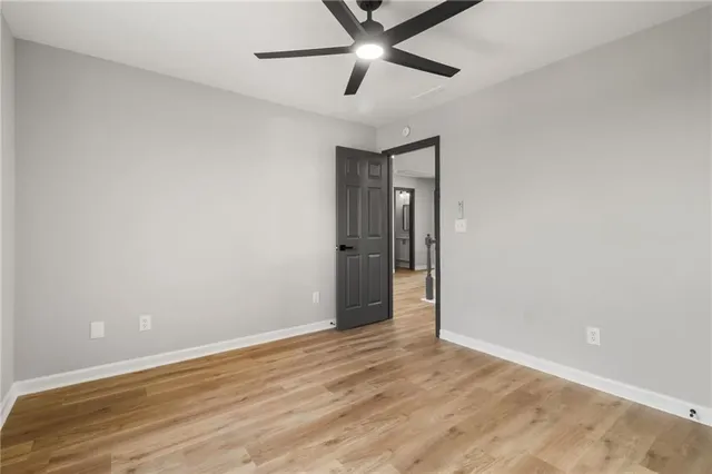 a view of an empty room with wooden floor and a ceiling fan