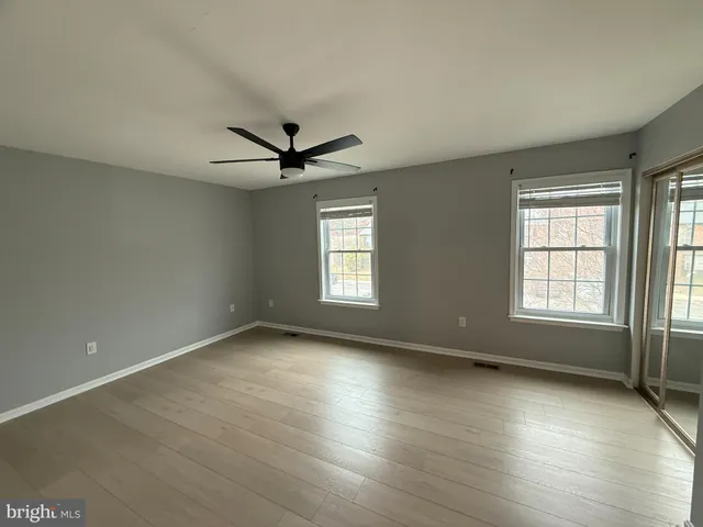 an empty room with wooden floor fan and windows