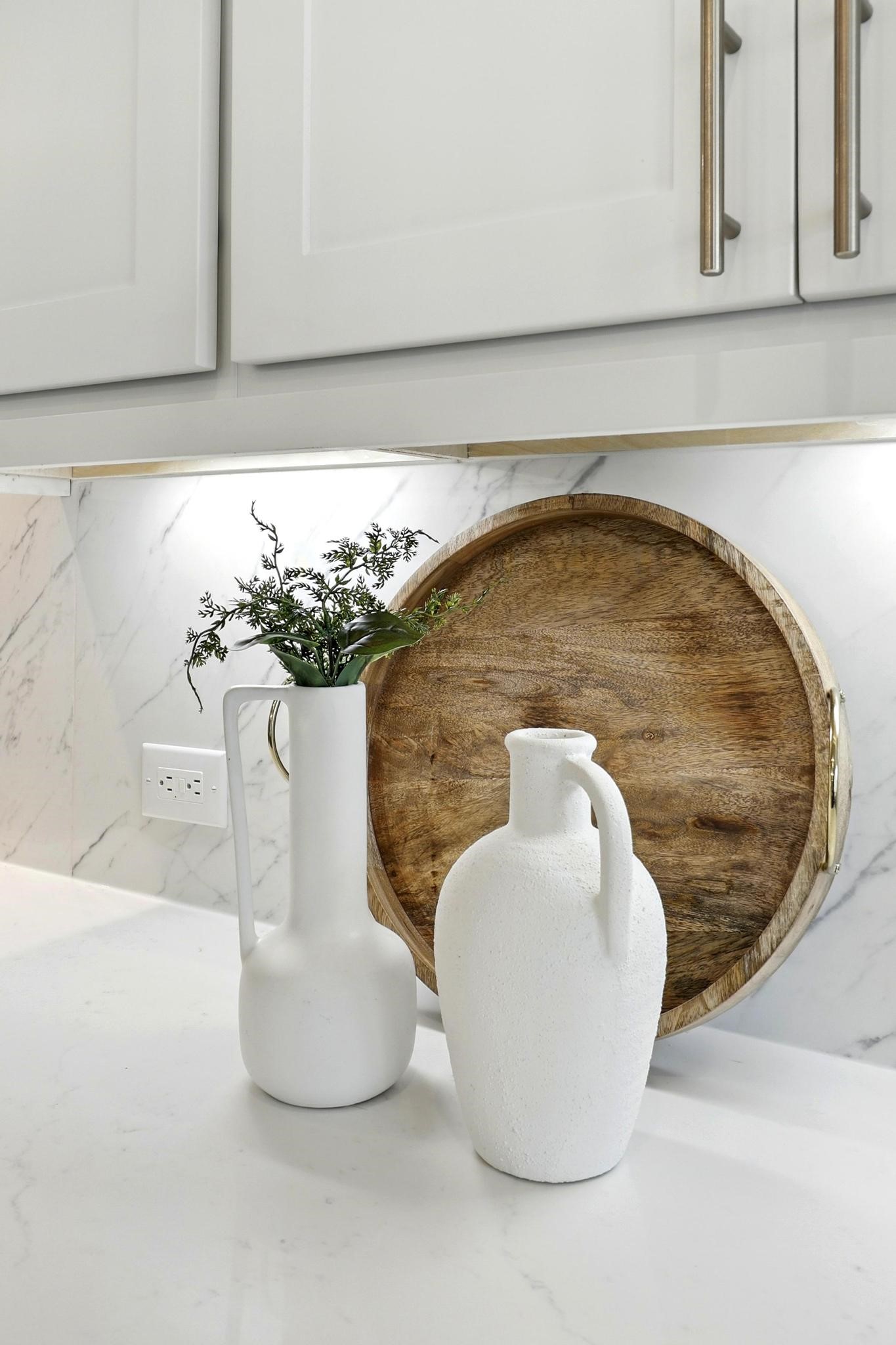 26923 Arethusa Court Spring, TX 77389 - Photo 24 of 44 This showcases a modern kitchen counter with a white marble backsplash, featuring elegant white vases and a decorative wooden tray. The sleek cabinetry and under-cabinet lighting add a sophisticated touch.