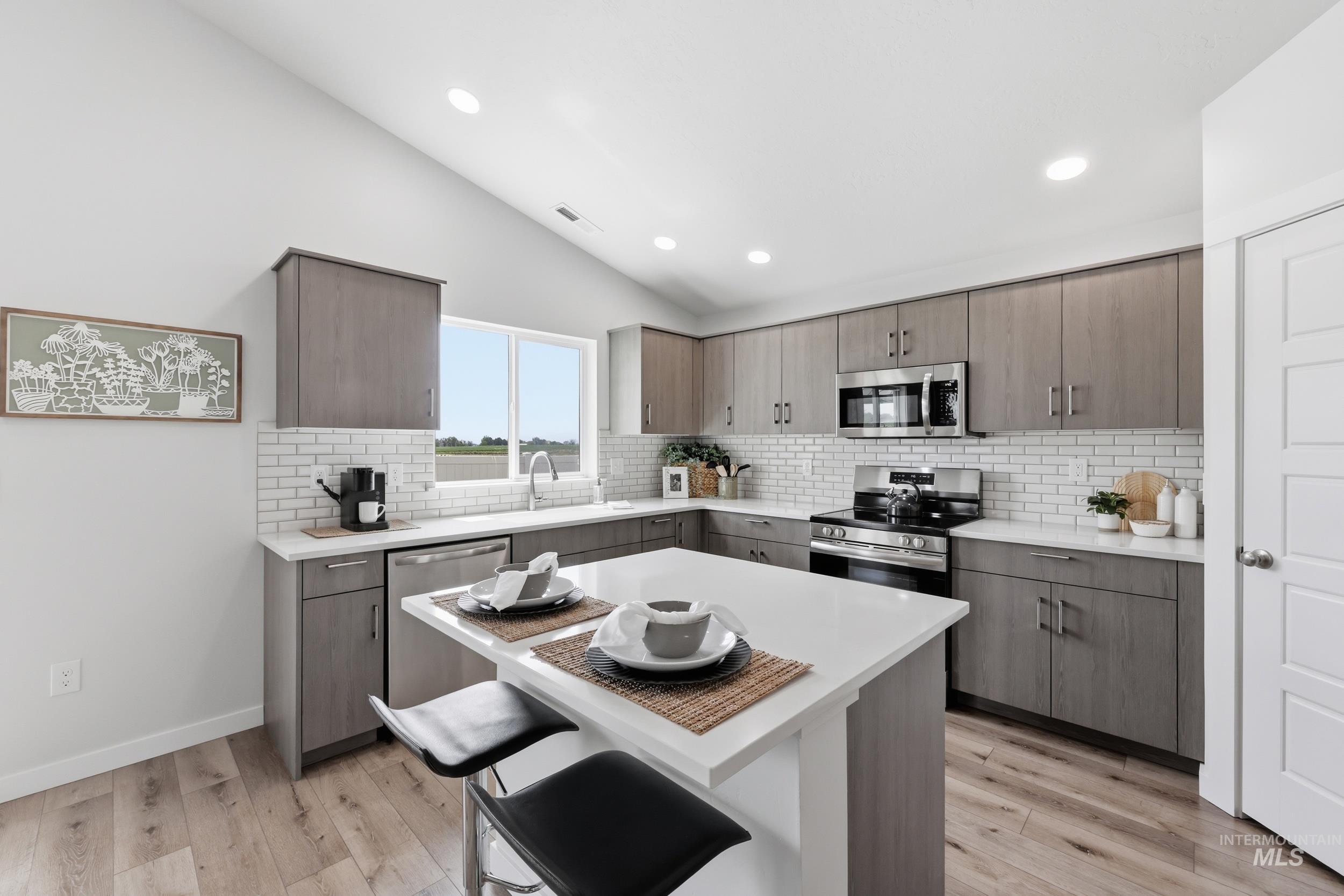 3665 W Lane Meridian, ID 83642 - Photo 6 of 42 Kitchen featuring wood-finish flooring, white subway tile backsplash, stainless steel appliances, a center island with countertop seating, and vaulted ceilings