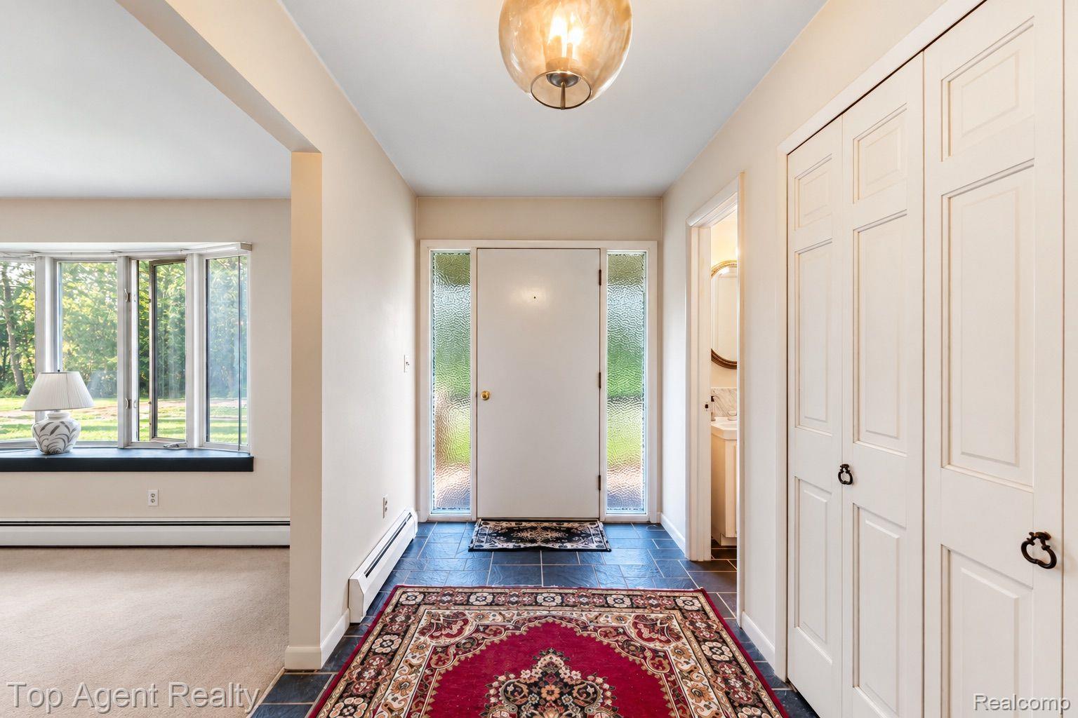 8269 Currie Road Northville, MI 48168 - Photo 2 of 80 Entry foyer featuring dark tile flooring, a statement ceiling light fixture, and a white front door with textured glass sidelights