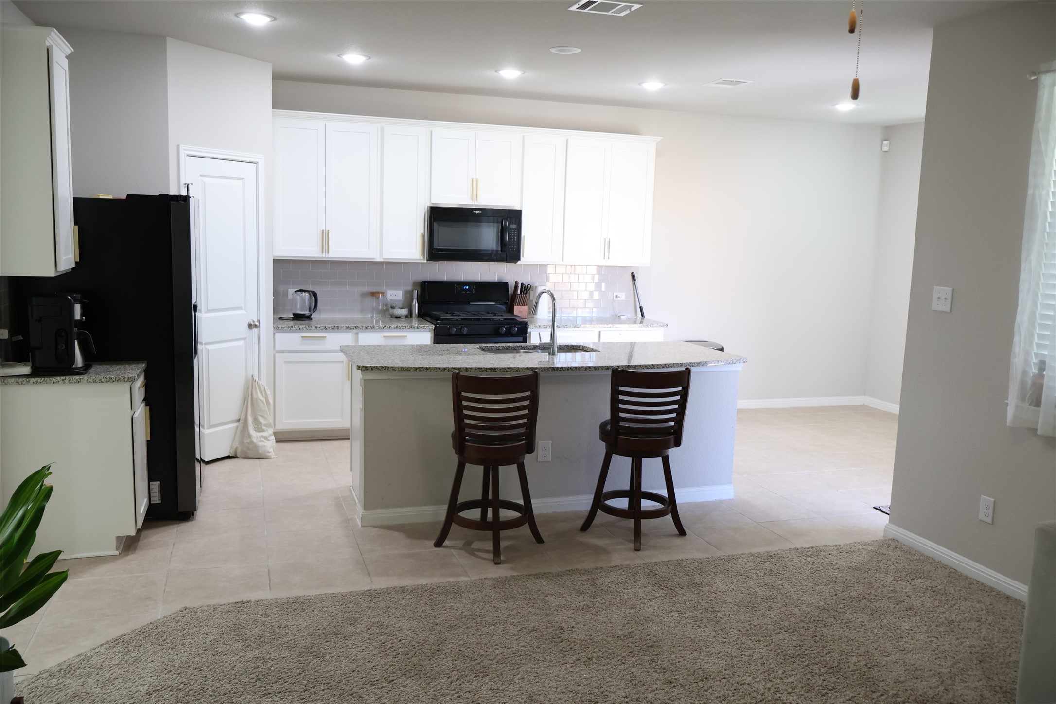11500 Maple Leaf Way Manor, TX 78653 - Photo 7 of 29 Kitchen featuring black appliances, a center island with sink, decorative backsplash, light tile patterned floors, and light stone countertops