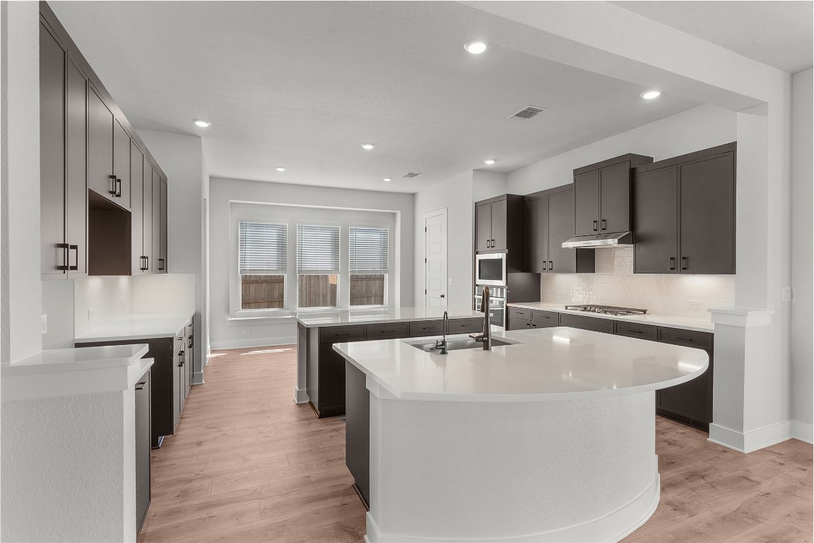 101 Golden Sage Avenue Georgetown, TX 78633 - Photo 3 of 24 Kitchen with decorative backsplash, recessed lighting, light wood-style flooring, light stone countertops, and stainless steel appliances