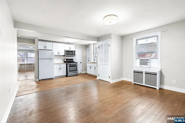 an empty room with wooden floor and a kitchen
