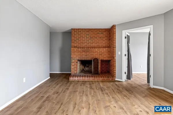 a view of an empty room with wooden floor fireplace and a window