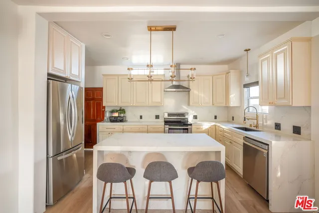 a kitchen with stainless steel appliances a stove a sink dishwasher a refrigerator white cabinets and wooden floor