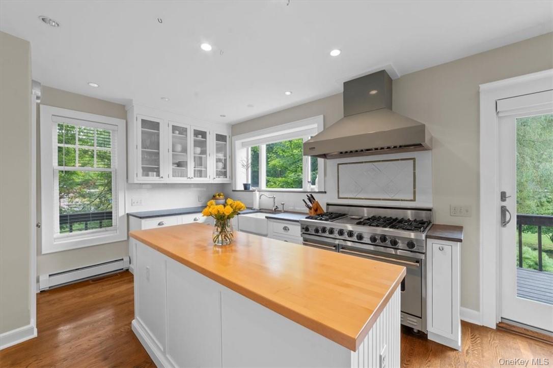 28 Inningwood Road Ossining, NY 10562 - Photo 17 of 37 Kitchen featuring range with two ovens, backsplash, light wood-type flooring, baseboard heating, and wall chimney exhaust hood