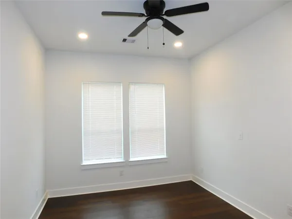 an empty room with wooden floor ceiling fan and windows