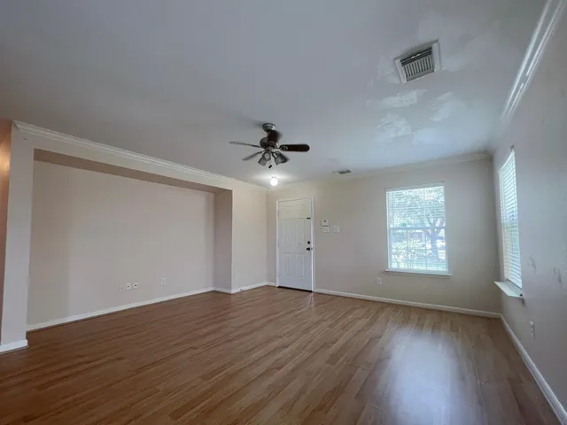 an empty room with wooden floor ceiling fan and windows