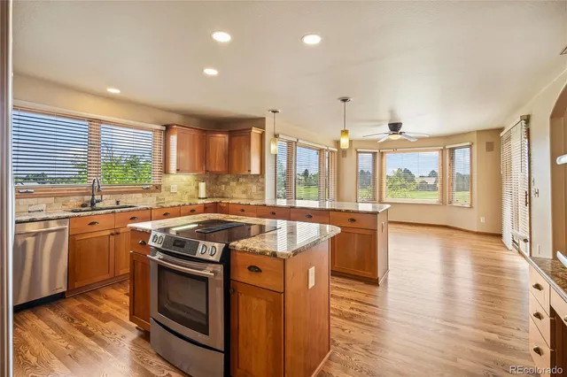 a kitchen with stainless steel appliances granite countertop wooden cabinets a stove a sink and a large window