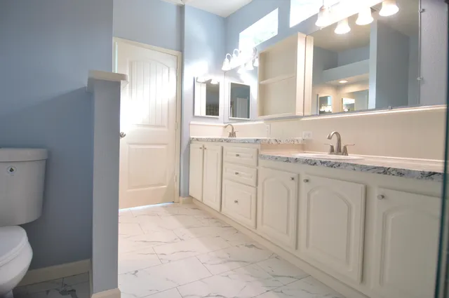 a spacious bathroom with a granite countertop sink a toilet and a mirror