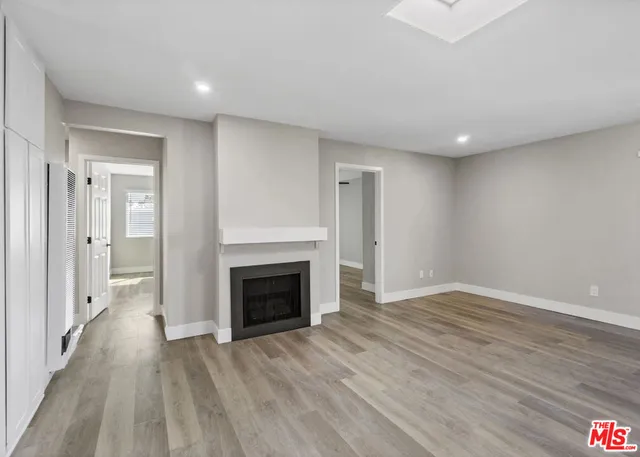 a view of an empty room with wooden floor fireplace and a window