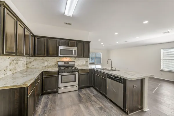 a kitchen with stainless steel appliances granite countertop wooden cabinets a sink dishwasher a stove and a refrigerator with wooden floor