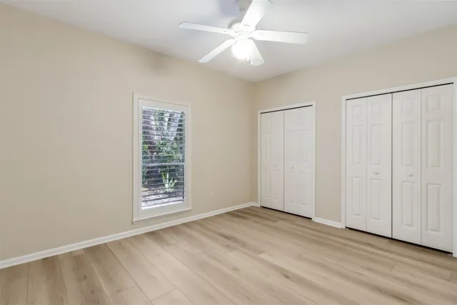 a view of an empty room with wooden floor and a ceiling fan