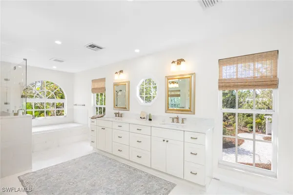 a spacious bathroom with double vanity a window a mirror a bathtub and windows