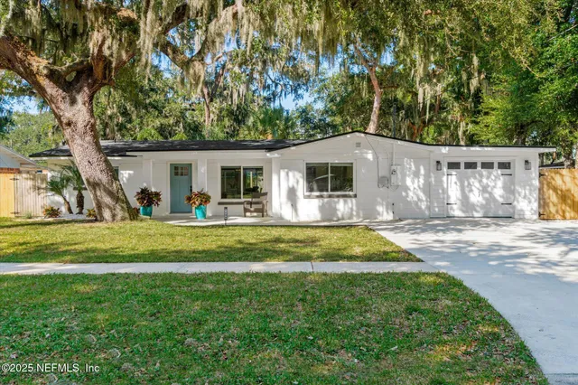 a view of a white house in front of a big yard with large trees