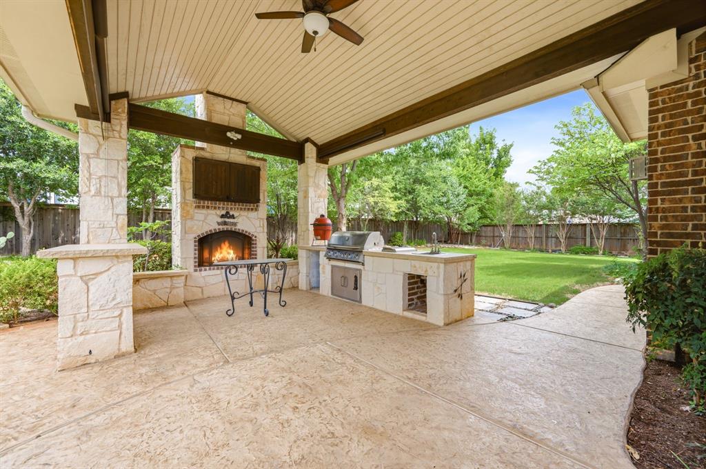 7013 Handel Colleyville, TX 76034 - Photo 3 of 37 Covered outdoor patio featuring a stone fireplace, built-in outdoor kitchen with grill and sink, stamped concrete flooring, and a ceiling fan