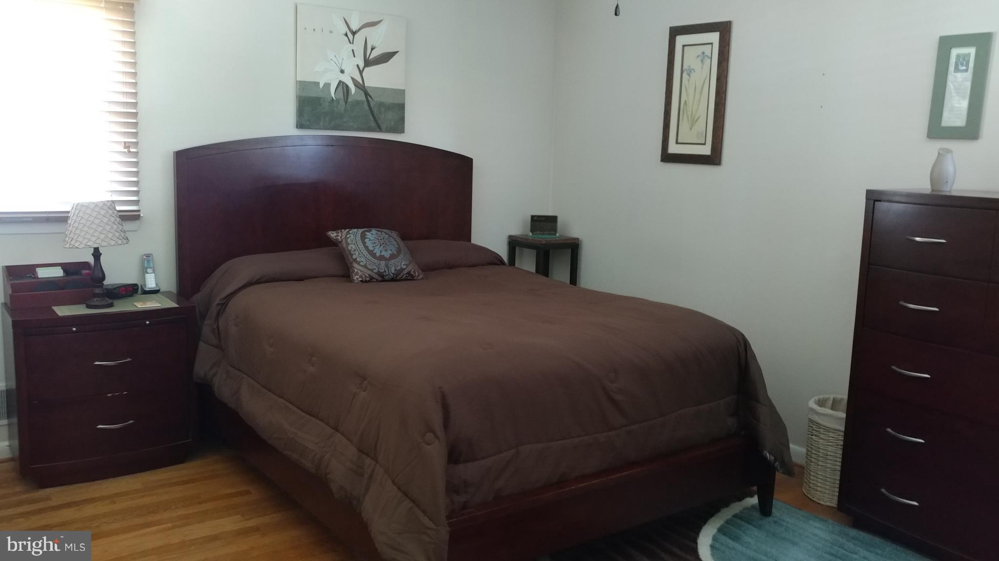 6002 Chesworth Road Baltimore, MD 21228 - Photo 8 of 26 a bedroom with a bed and a lamp on dresser