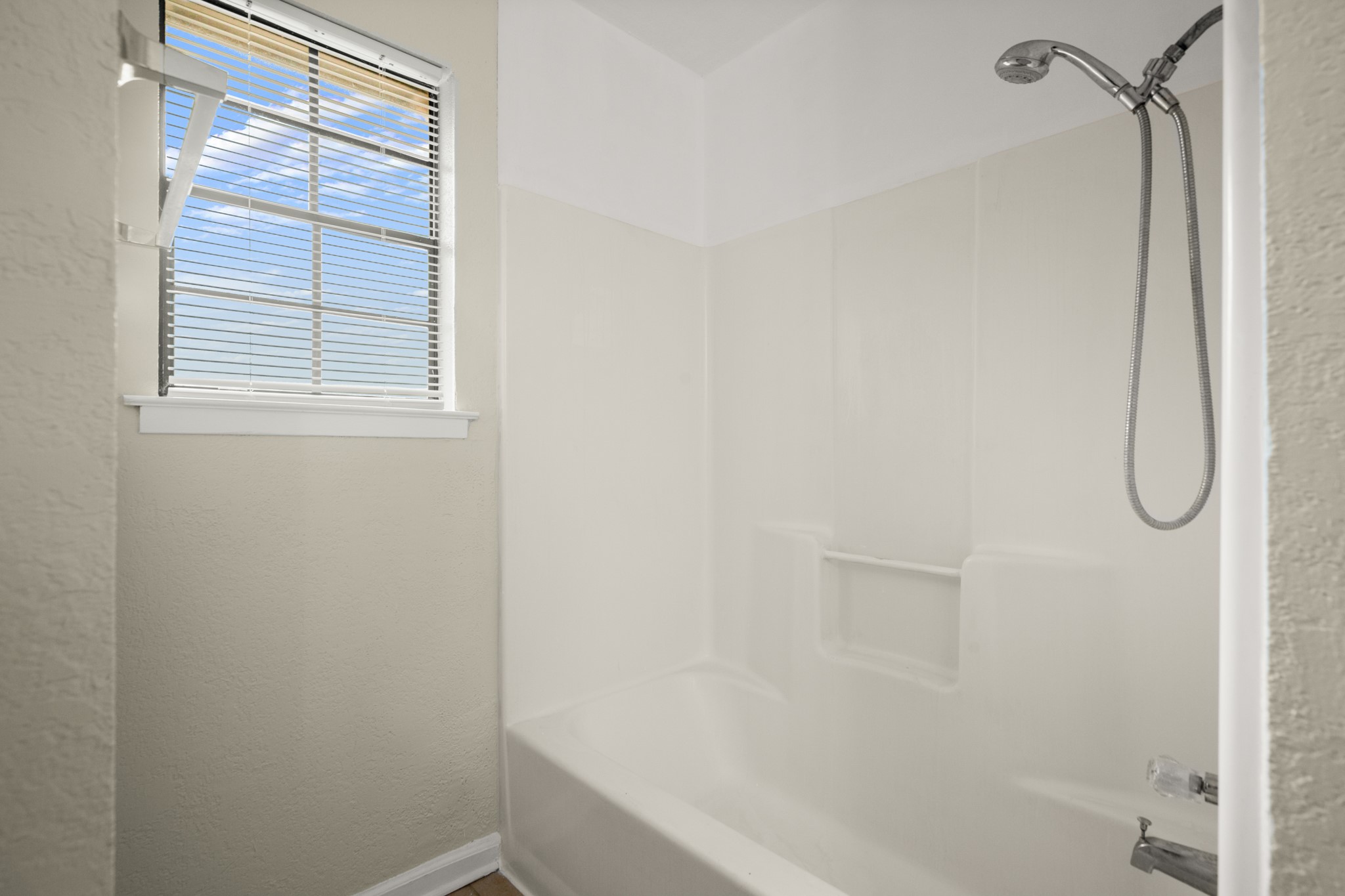 3801 Foust Trail, Unit B Georgetown, TX 78628 - Photo 18 of 31 The bathroom features a window with blinds, a shower-over-bath unit, and a chrome shower head with a flexible hose