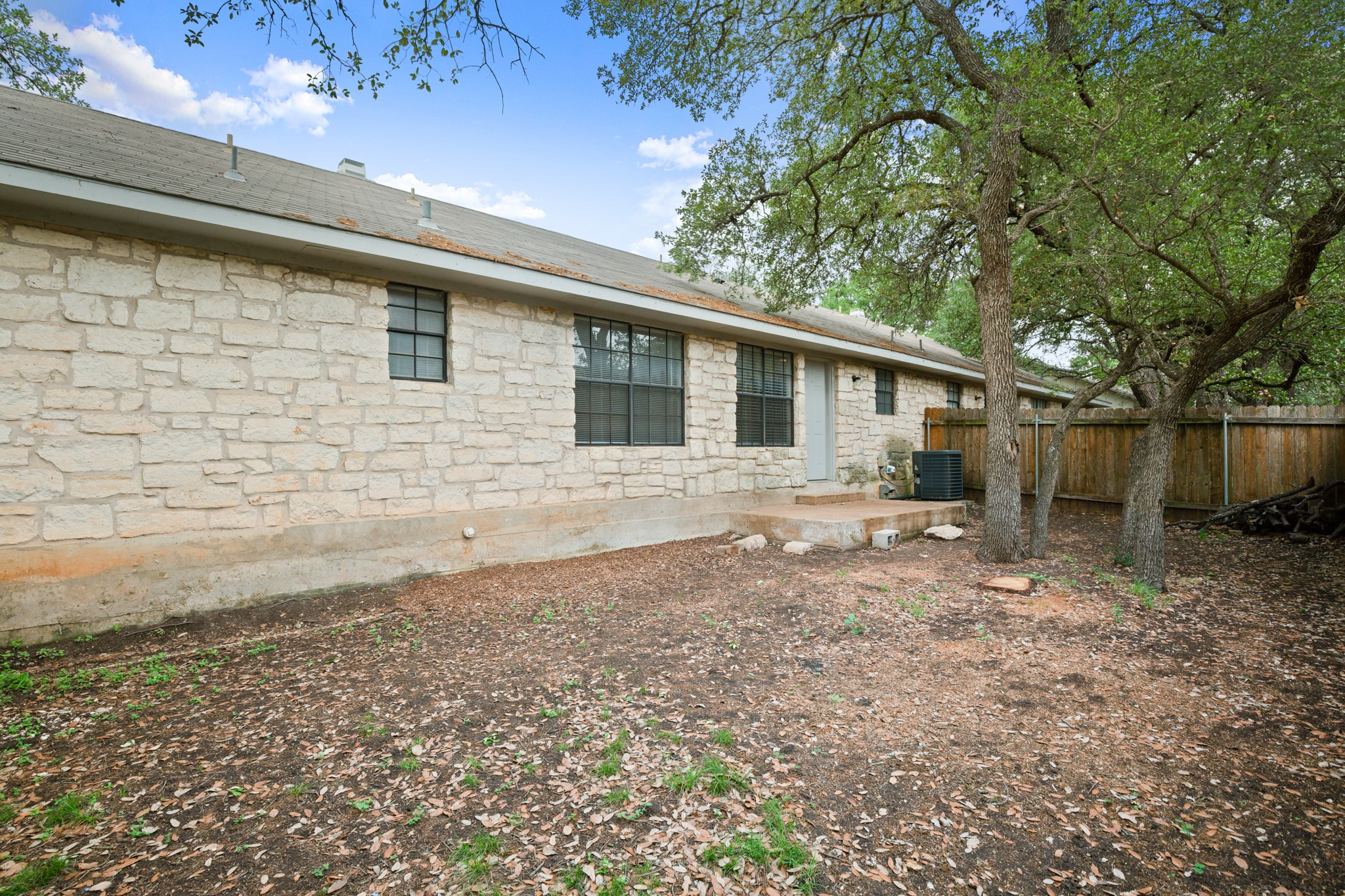 3801 Foust Trail, Unit B Georgetown, TX 78628 - Photo 25 of 31 The property features a stone exterior with multiple windows, a grey roof, and a back door leading to a concrete patio