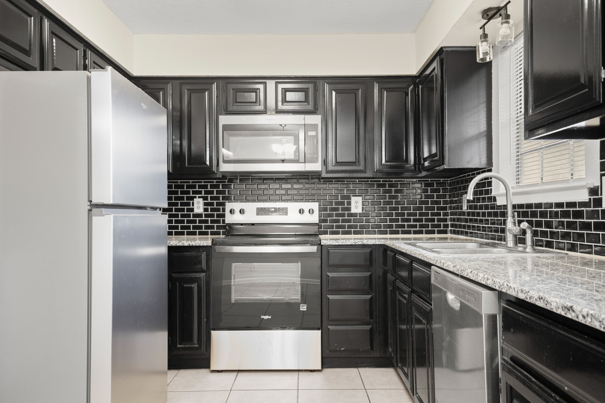 3801 Foust Trail, Unit B Georgetown, TX 78628 - Photo 6 of 31 The kitchen features dark cabinetry, stainless steel appliances, a black subway tile backsplash, and light-colored granite countertops