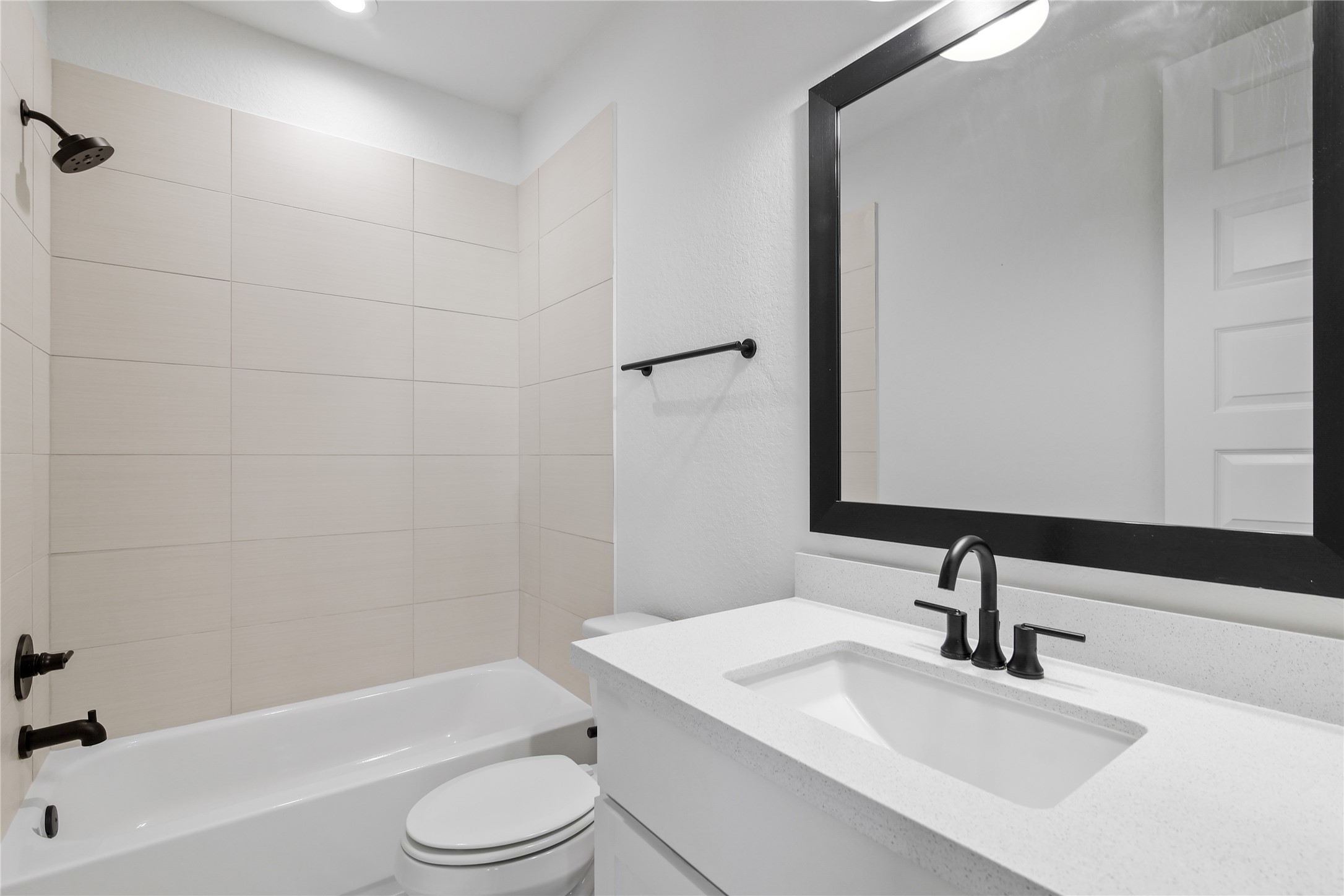 4231 Allen Street Houston, TX 77007 - Photo 19 of 31 This modern en suite pairs white shaker cabinets and quartz counters with bold matte black hardware for a high-contrast look. Warmth is added through large-format, sand-beige shower tiles laid in a clean horizontal pattern.