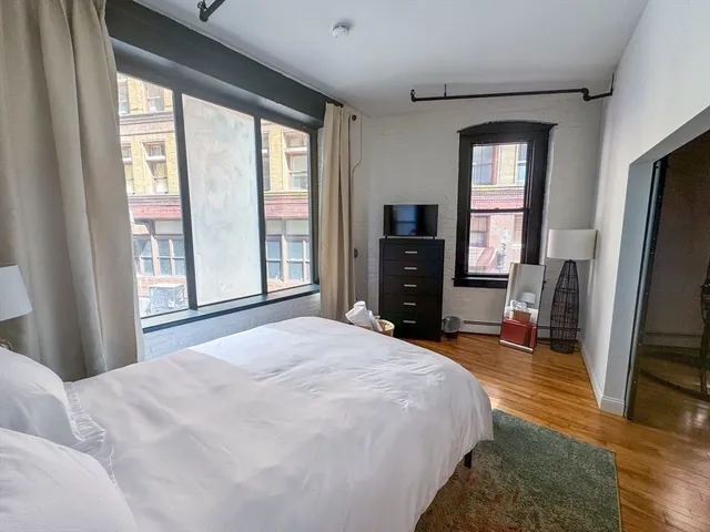 a bedroom with a bed dresser and a flat tv screen next to a window