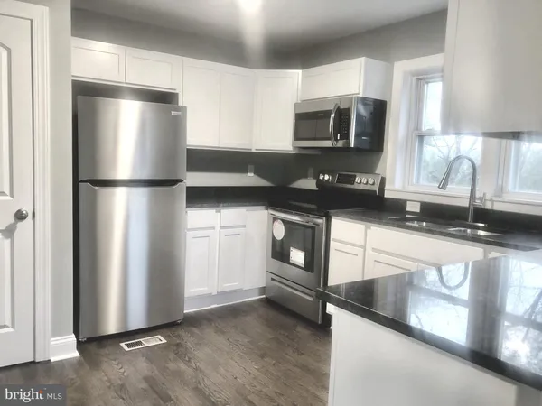 a kitchen with stainless steel appliances granite countertop a refrigerator a stove a sink and white cabinets