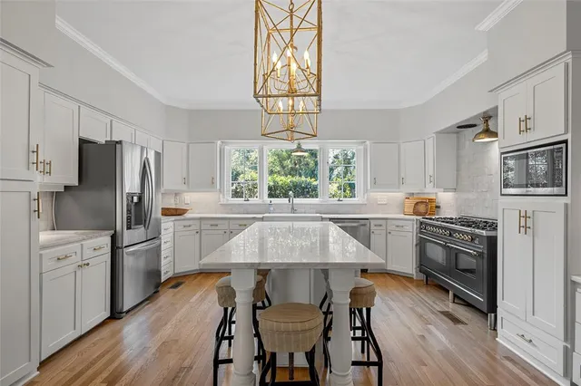 a kitchen with stainless steel appliances a stove a sink dishwasher a refrigerator cabinets and dining table with wooden floor