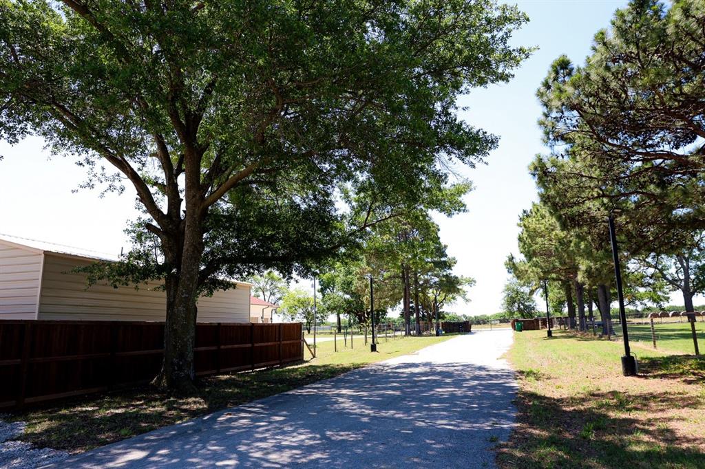 10575 Friendship Road Pilot Point, TX 76258 - Photo 32 of 32 Paved driveway featuring mature trees, a wood privacy fence, and a white siding structure