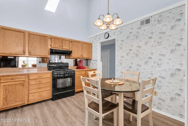 a kitchen with stainless steel appliances granite countertop a stove a refrigerator a sink a dining table and chairs with wooden floor