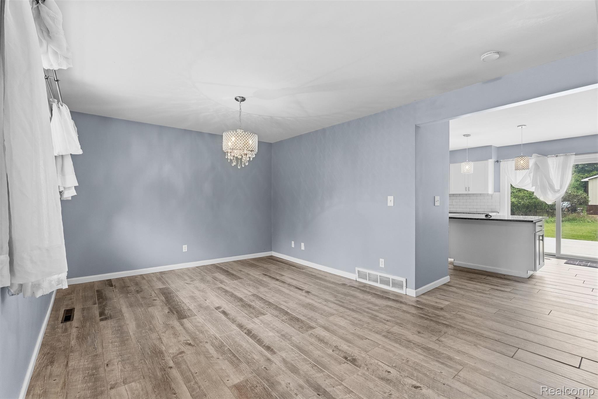 819 Alpine Trail Fenton, MI 48430 - Photo 6 of 41 Wood-finish flooring throughout, complemented by a crystal chandelier, and an open layout to a kitchen featuring white cabinetry and pendant lighting