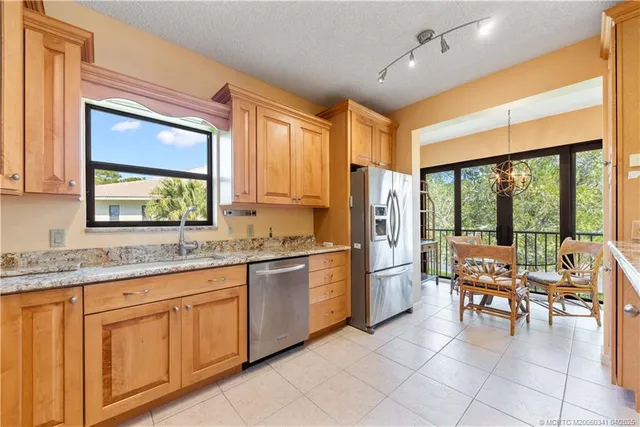 a open kitchen with stainless steel appliances granite countertop a stove top oven a refrigerator a dining table and chairs with the outer view