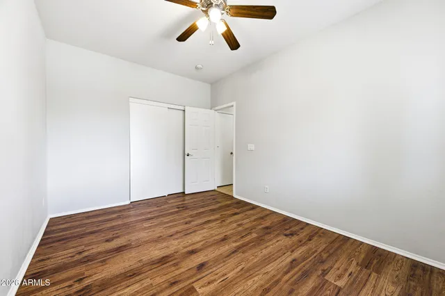 an empty room with wooden floor ceiling fan and windows