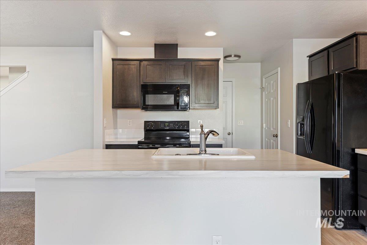 926 West Woodpine Street Meridian, ID 83646 - Photo 8 of 32 Kitchen with black appliances, light countertops, a center island with sink, dark brown cabinetry, and recessed lighting