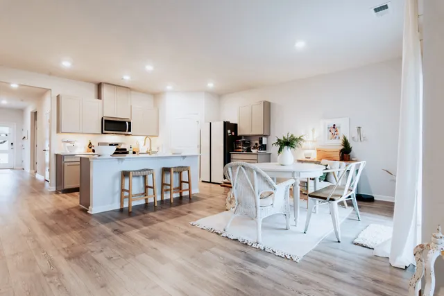 a kitchen with stainless steel appliances granite countertop a stove top oven a sink a dining table and chairs with wooden floor